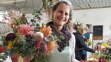 Frau hält bunte Blumenstrauß in einem blumenreichen Raum.